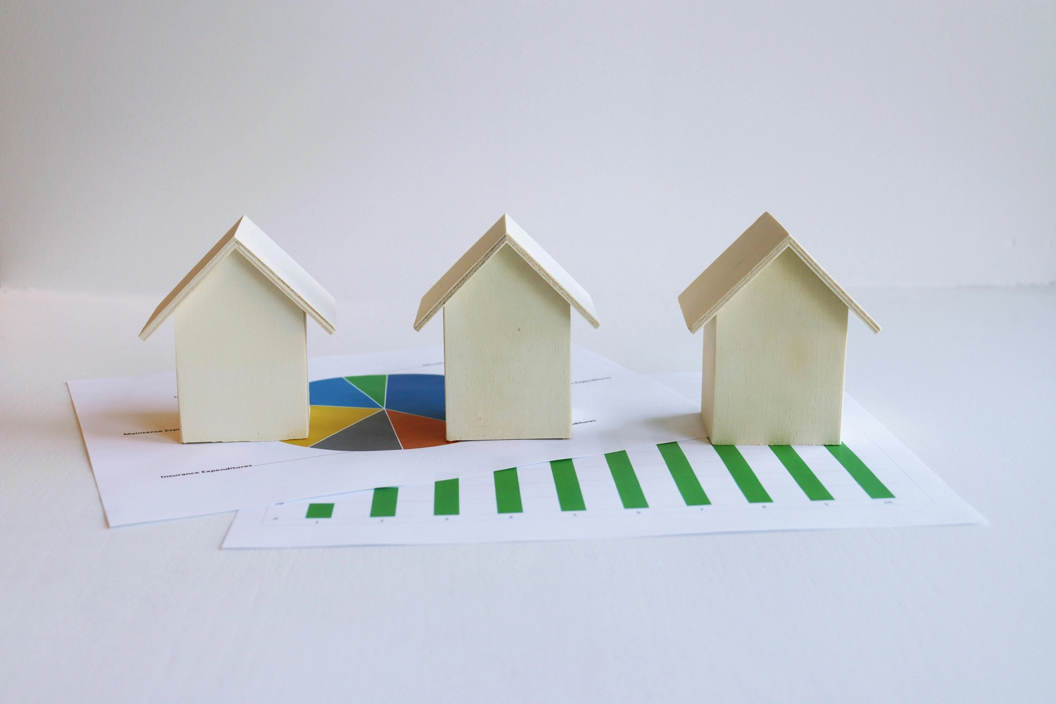 Roland Renner GmbH - Immobilienverwaltung und Gebäudedienstleistungen - Drei kleine Holzhausmodelle stehen auf ausgedruckten Finanzdiagrammen.